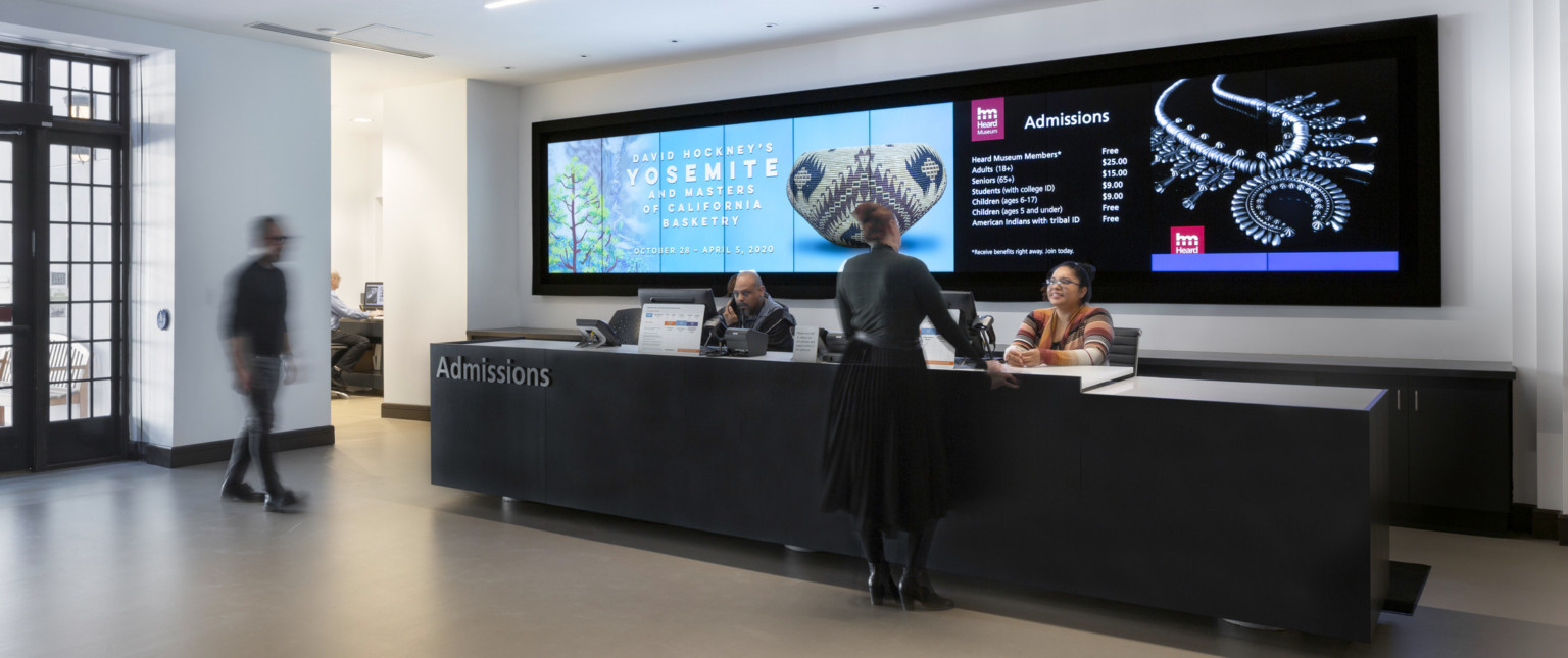 A large black admissions desk with a screen behind listing admission prices and exhibition announcements