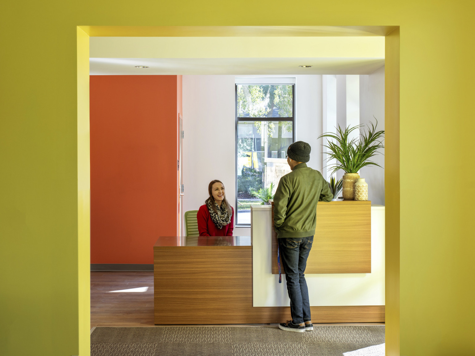 Wood desk with white partition at building entry in a room with white and orange walls, framed by yellow doorframe