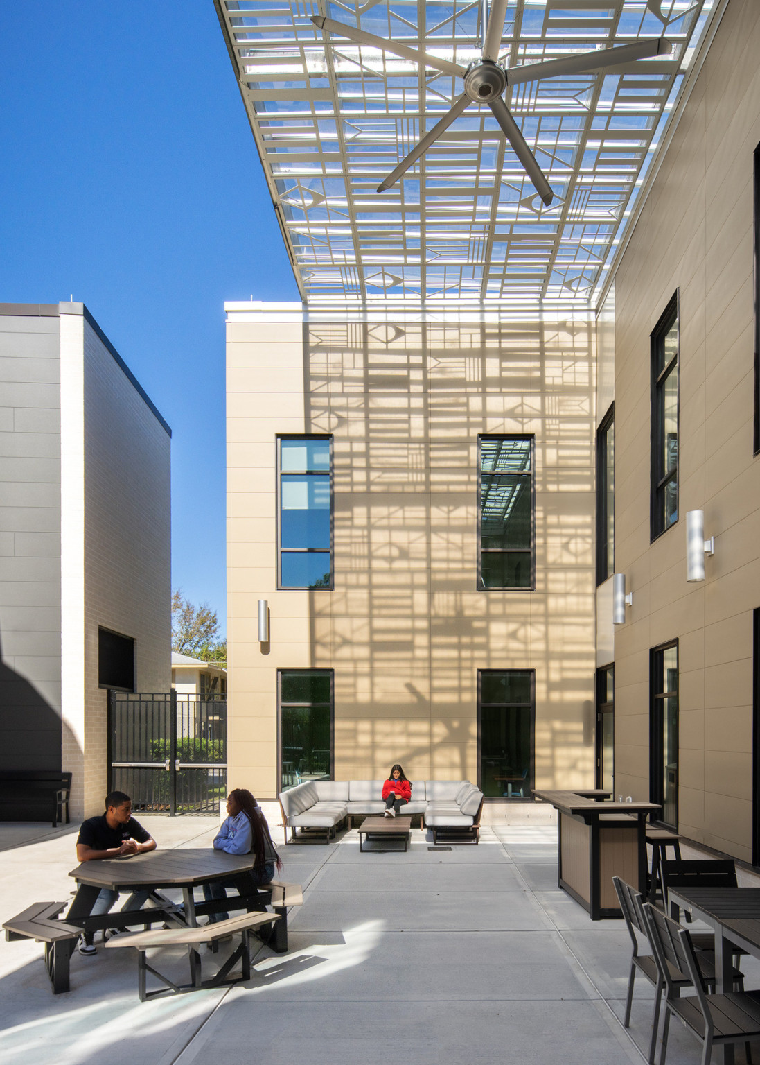 A courtyard between the 2 buildings with seating areas. The partially translucent awning creates geometric shadows