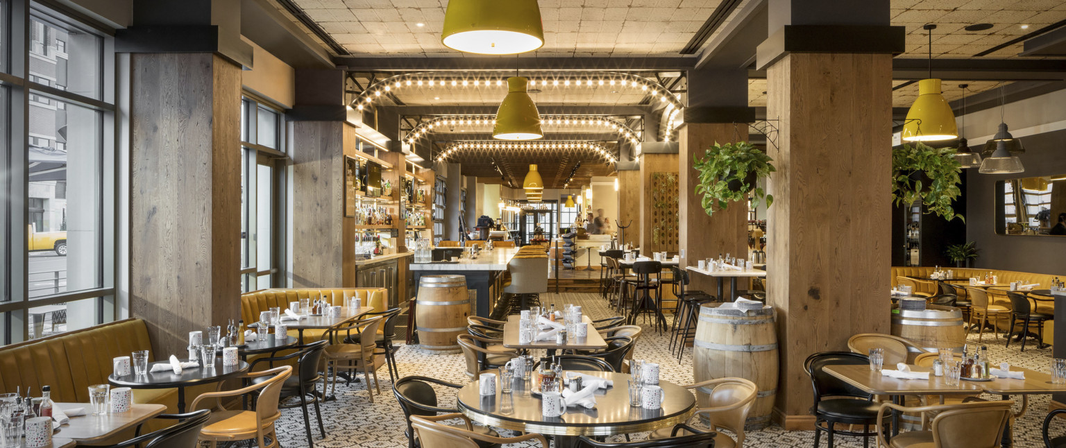Dining area with illuminated metal archways between wood pillars. Yellow booths along left wall and neutral toned seating