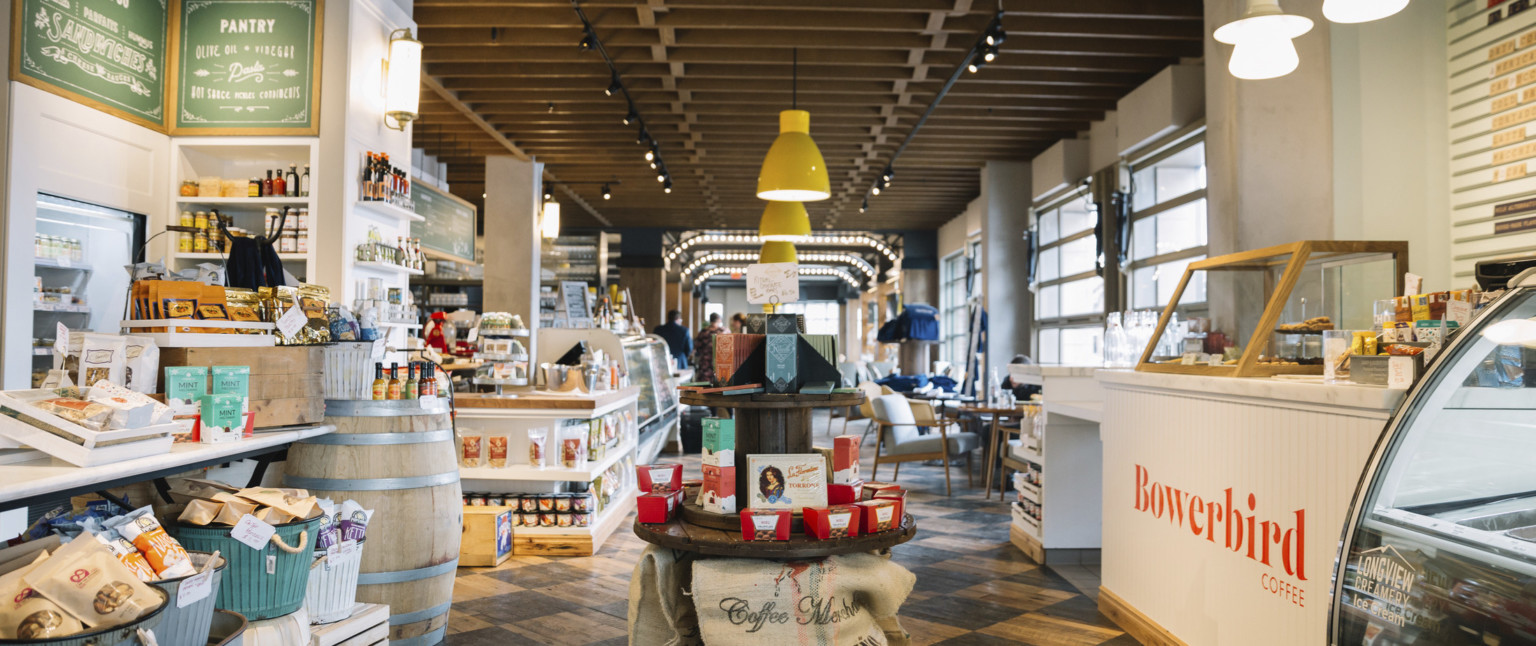 Round wood display with candy in a shop next to white counter with Bowerbird Coffee sign to right. Wood floor and ceiling