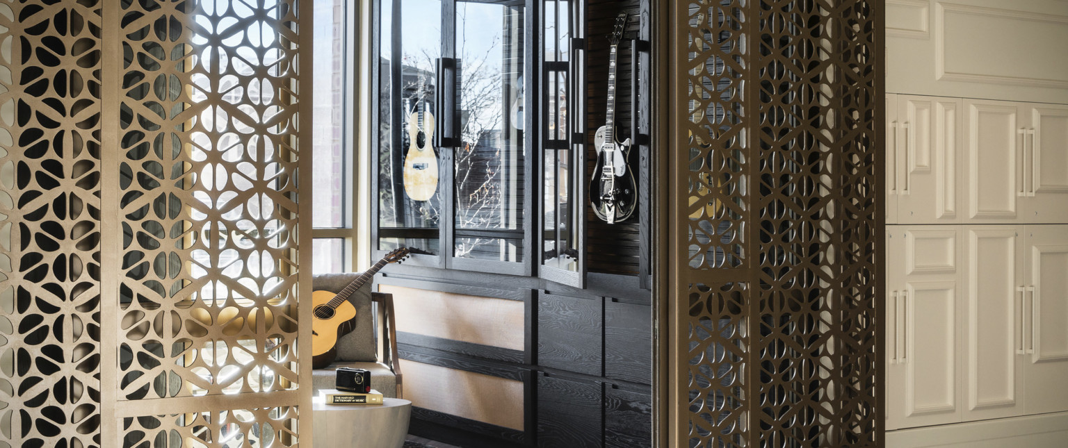 Organic shaped translucent metallic doorframe wraps around opening to room with black, glass door cabinet holding guitars