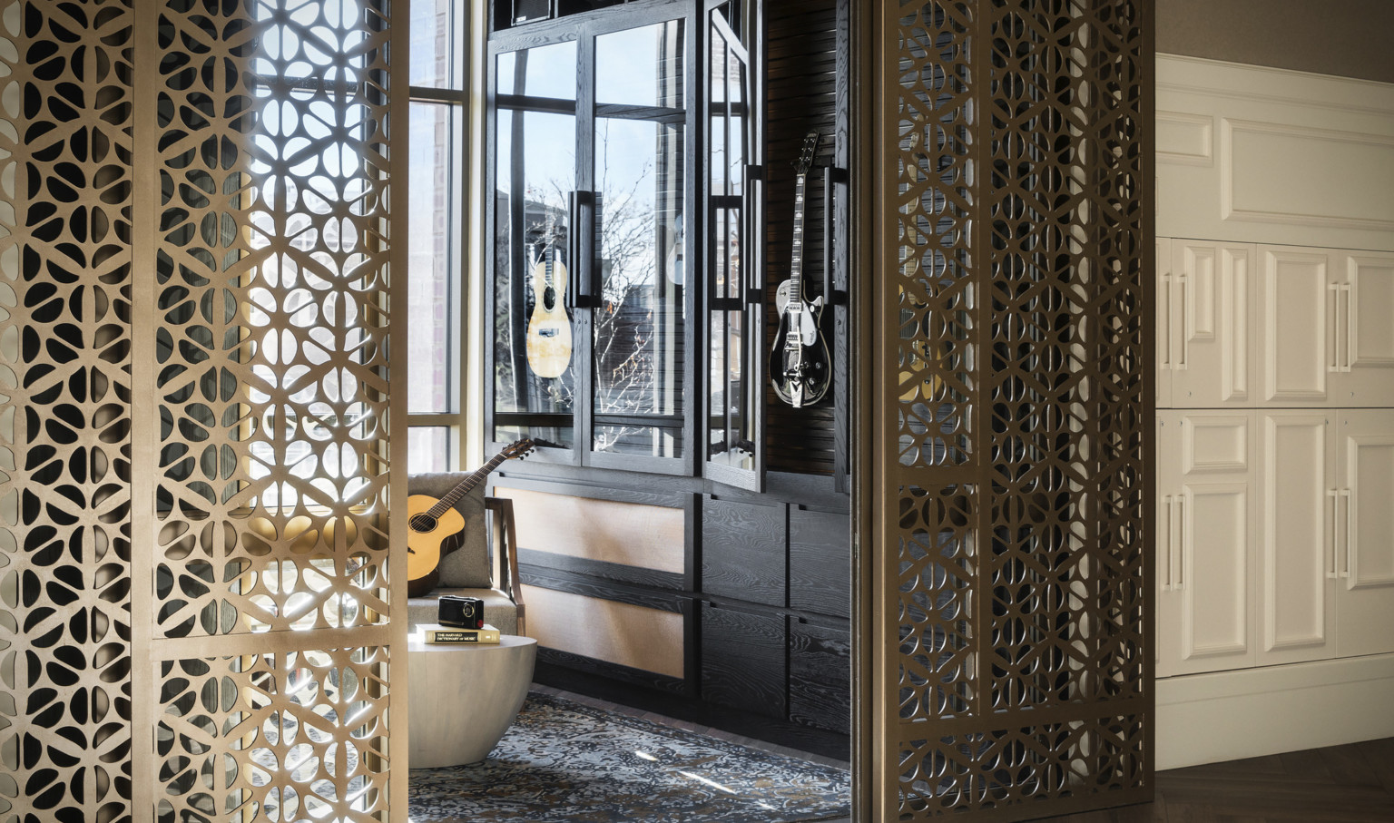 Organic shaped translucent metallic doorframe wraps around opening to room with black, glass door cabinet holding guitars