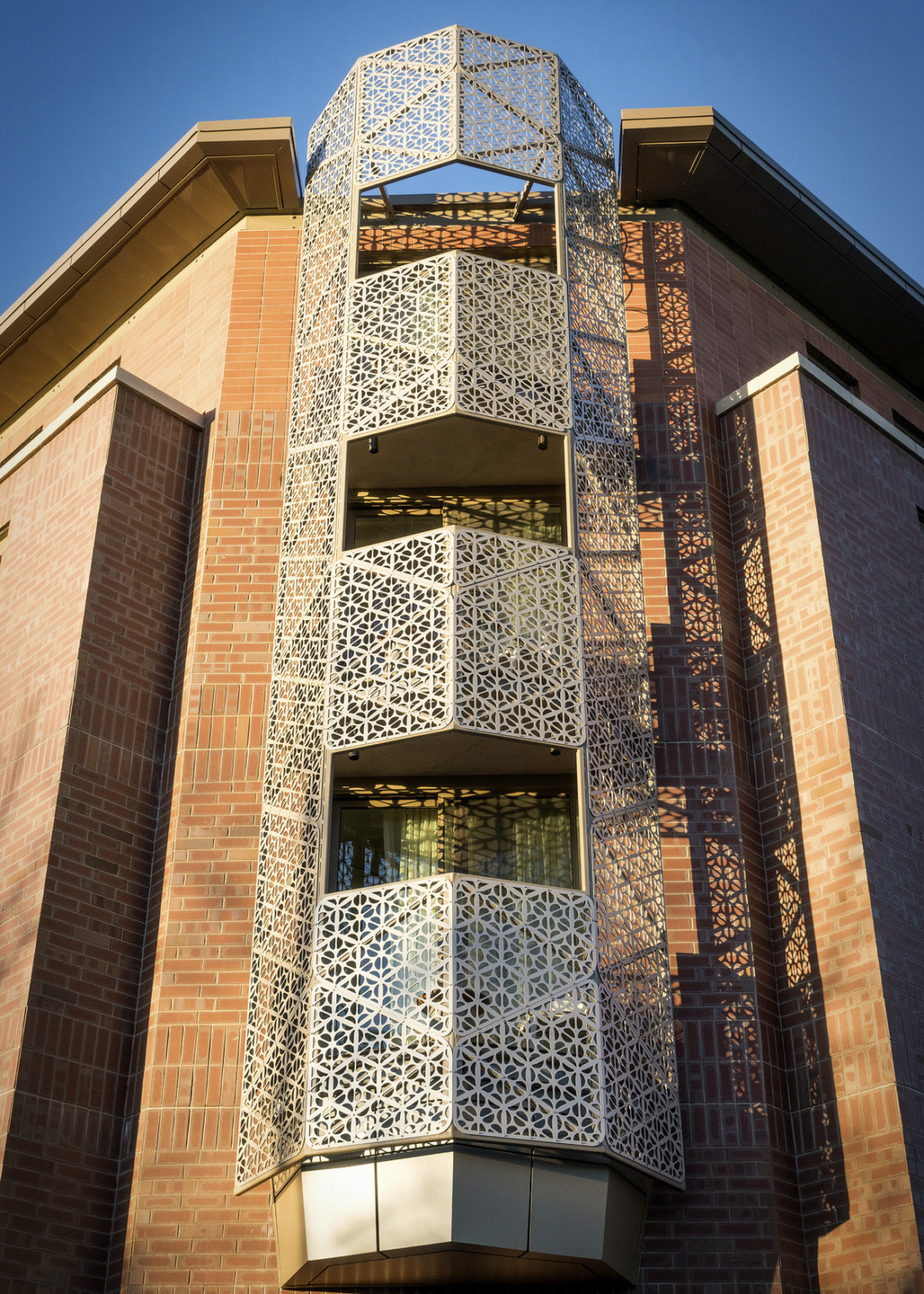 The metal with organic cutouts wraps around 3 exterior corner balconies as bannisters and multistory tower on brick building
