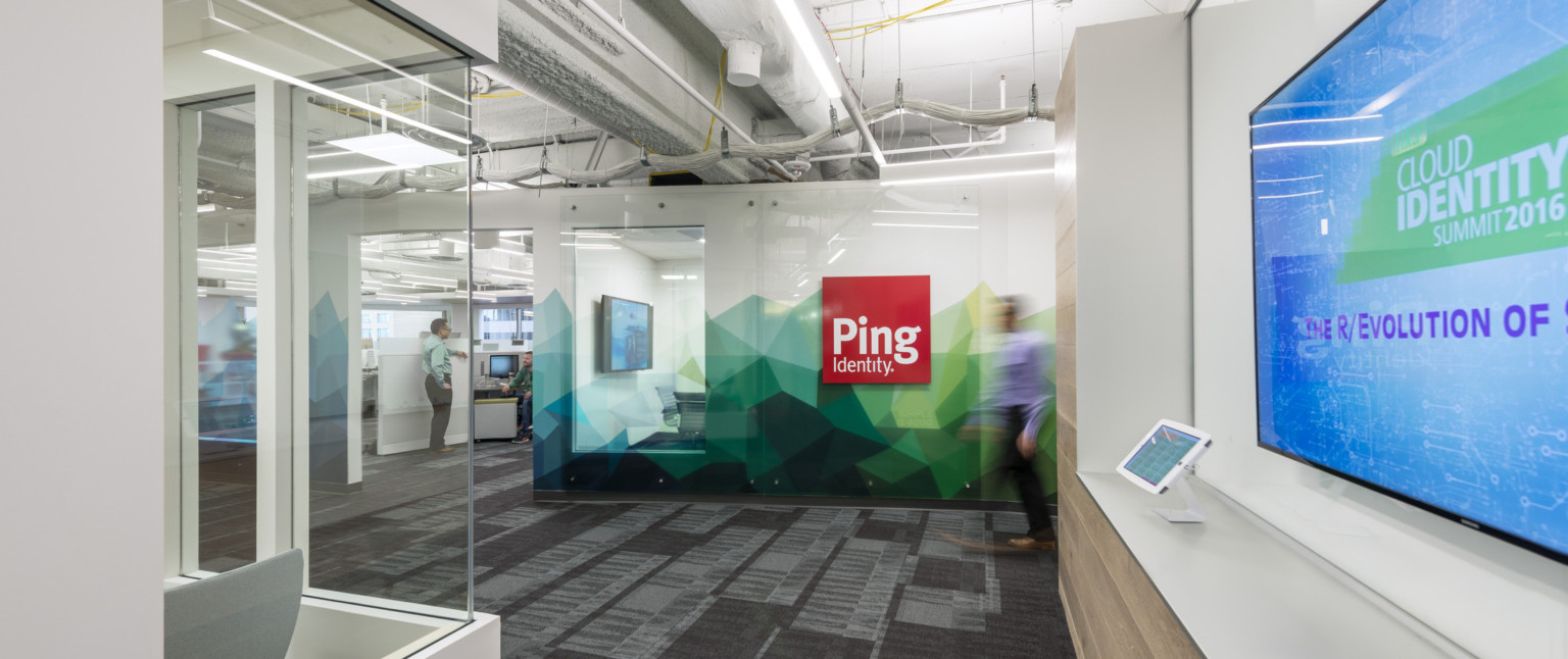 Hallway facing sign for Ping Identity on white wall with angular abstract green and blue mural along base
