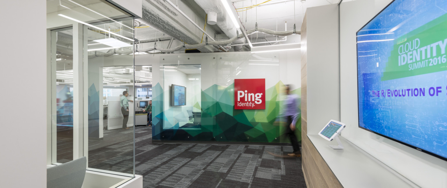 Hallway facing sign for Ping Identity on white wall with angular abstract green and blue mural along base Hallway facing sign for Ping Identity on white wall with angular abstract green and blue mural along base