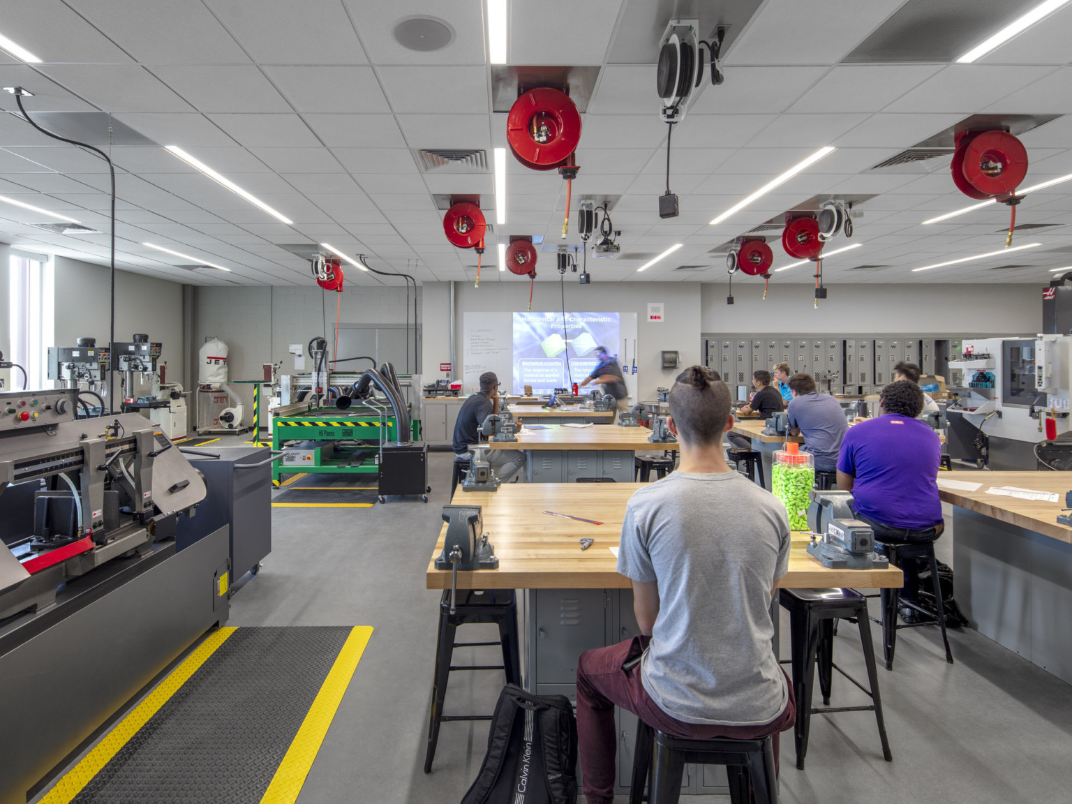 Classroom with equipment along left wall. Tables and stools in rows, right, with extension cords dispensed from above