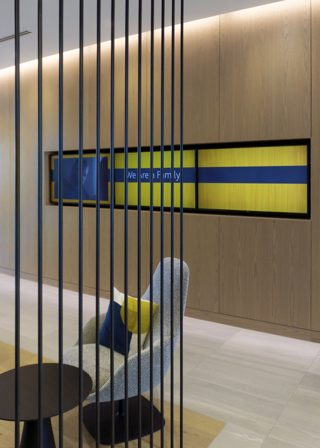 Hallway with wood wall and recessed blue and yellow panel across from seating behind black metal bar partition