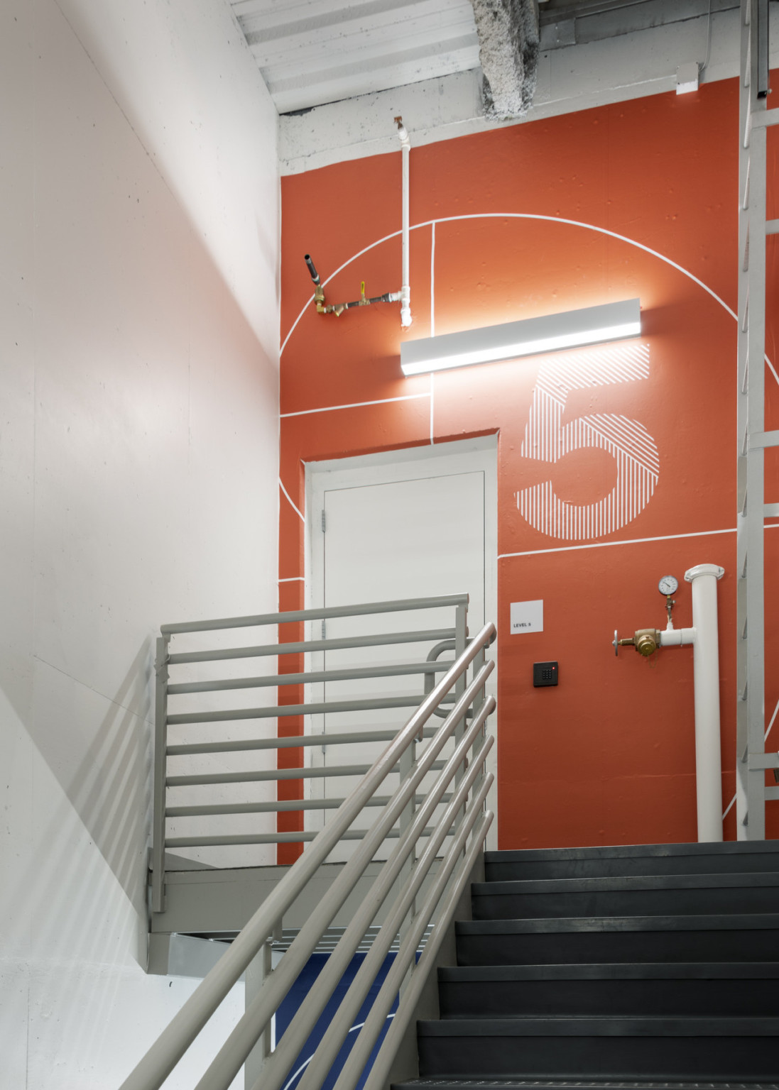 Orange wall mural with patterned number 5 next to white door at top of black staircase with white railing