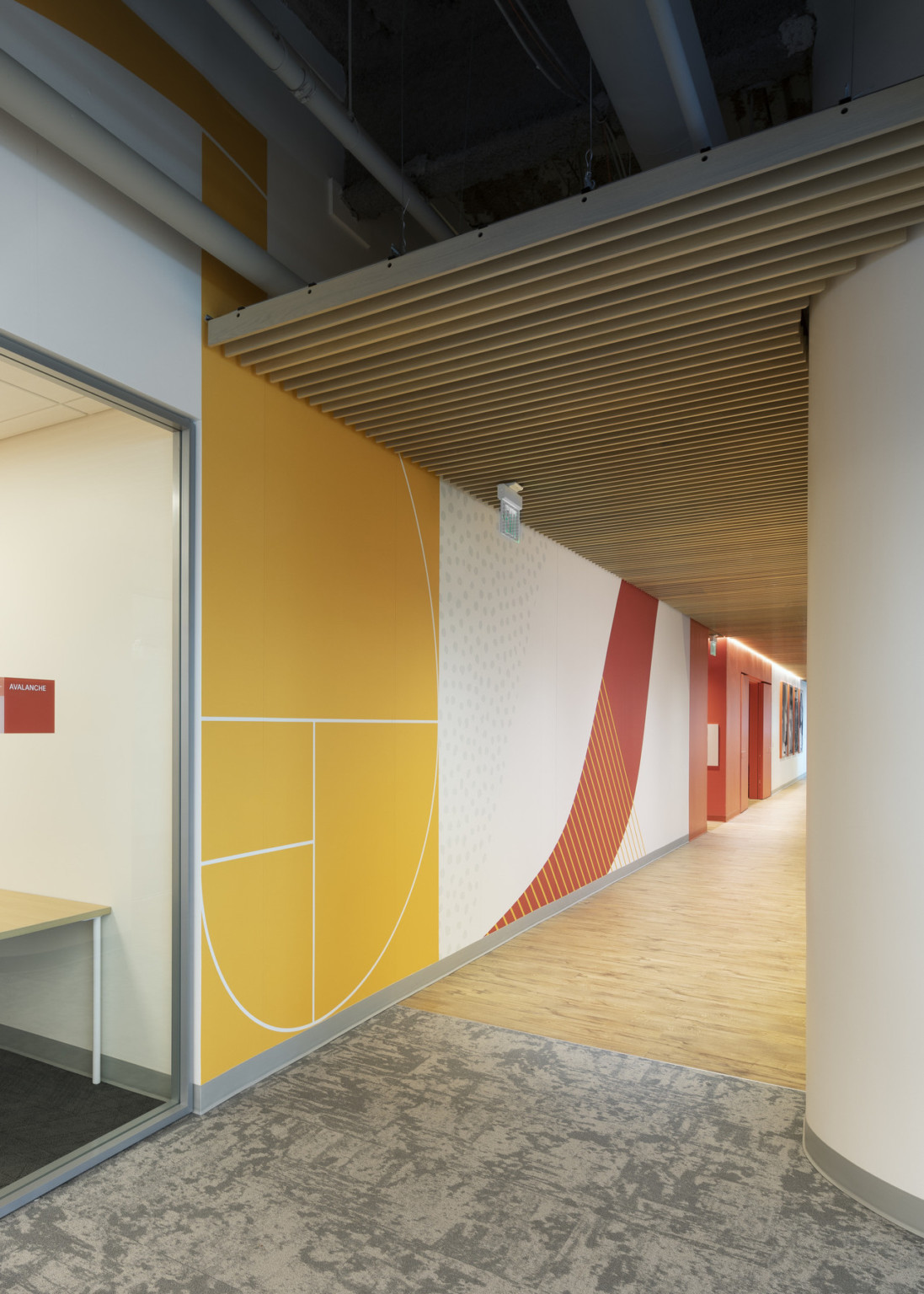 Entrance to hallway with orange, white, and yellow abstract mural on left wall below wood slat drop ceiling