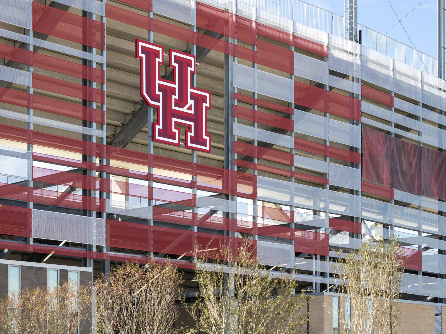 Closeup of UH logo on red and white sunscreen facade of stadium with view of the stepped underside of bleachers