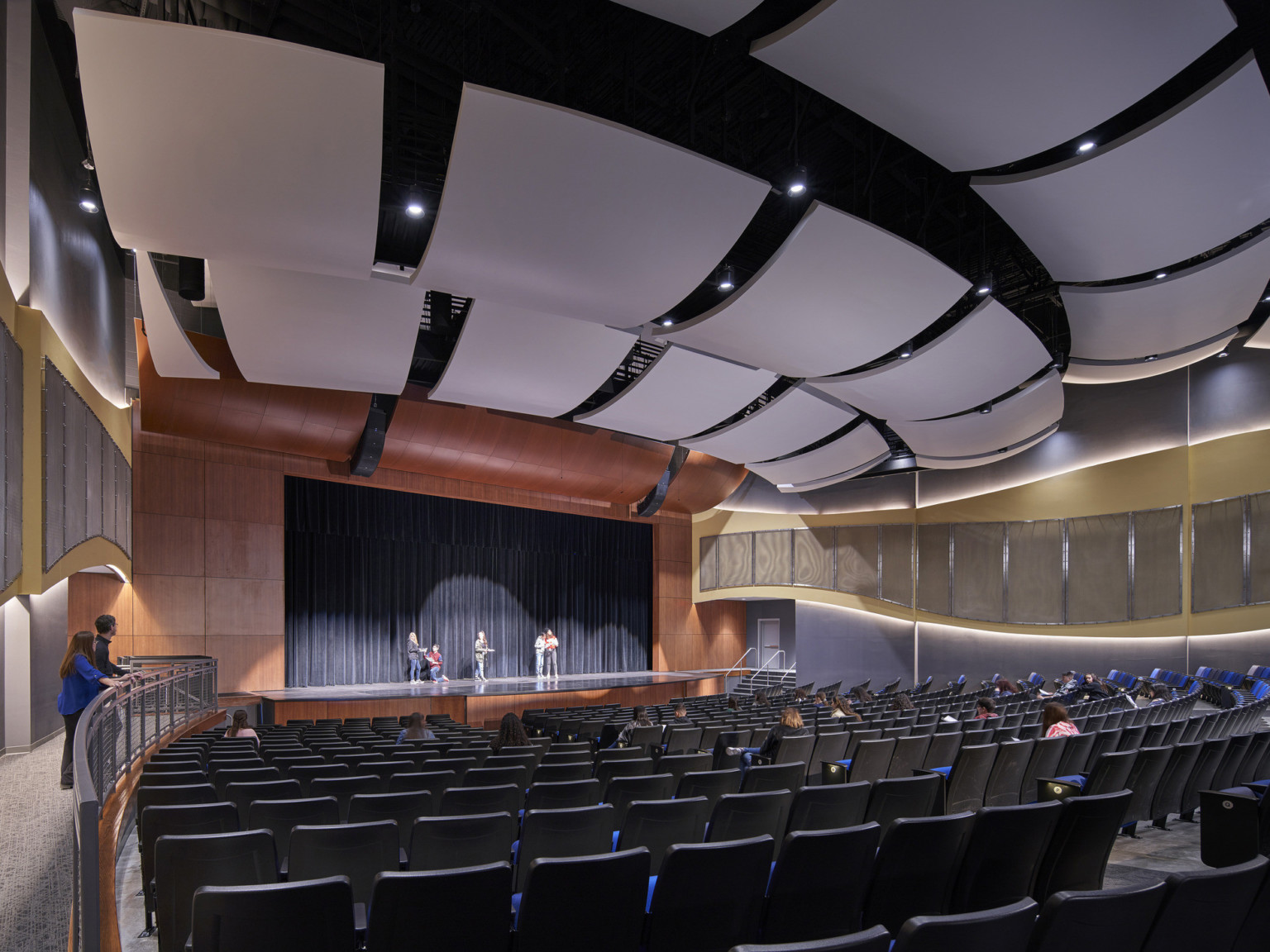 View of theater from back, facing stage with rounded wood framing. Rows of acoustical panels above and along wood side walls
