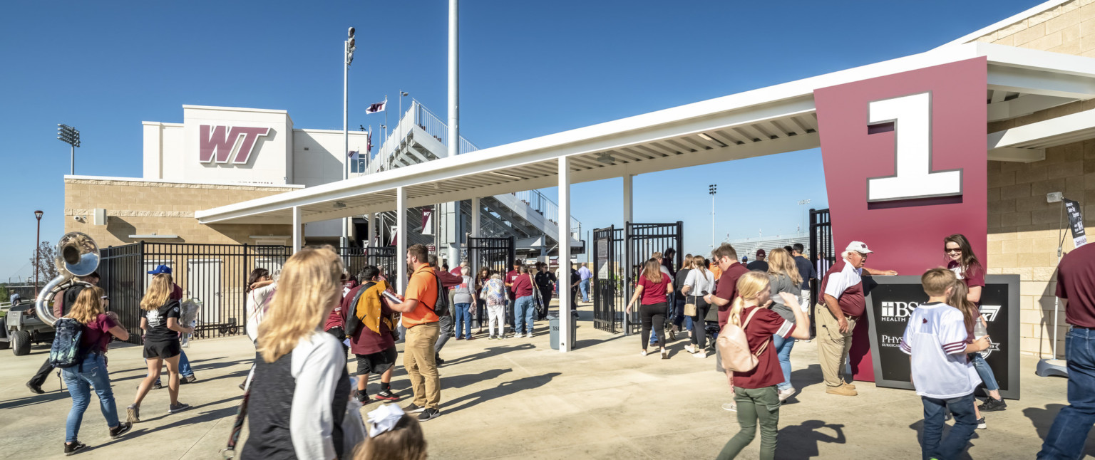 Gated entrance to stadium labeled 1 in white font on red angled panel to right. Canopy over entry connecting to building