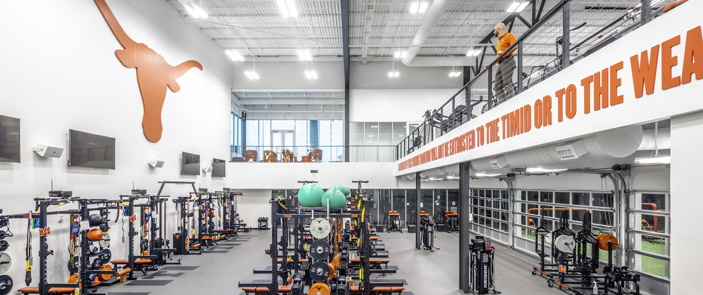 Looking down center row of equipment in double height white room. Screens and orange longhorn mascot logo on left wall