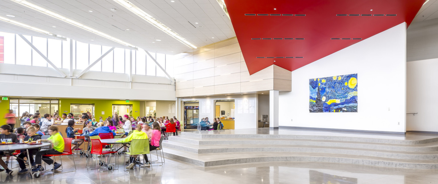 Double height cafeteria with angled red accent connecting with wood paneled wall. Van Gogh's Starry Night hangs by platform