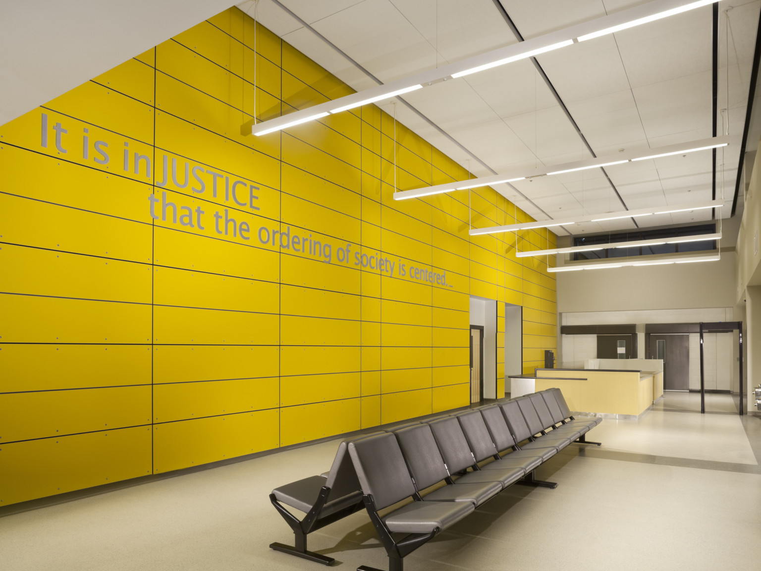 Seating area in lobby with yellow accent wall. A sign on wall reads It is in JUSTICE that the ordering of society is centered