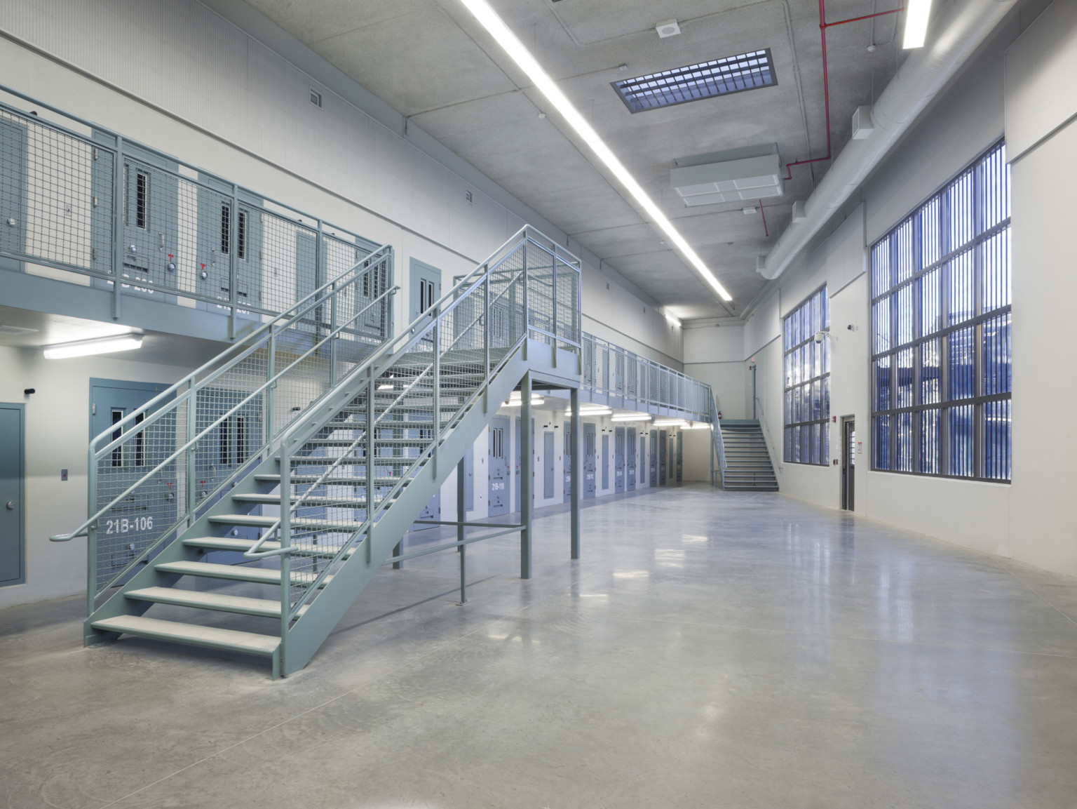 Two floors of cells with grey doors open into central area with large barred windows