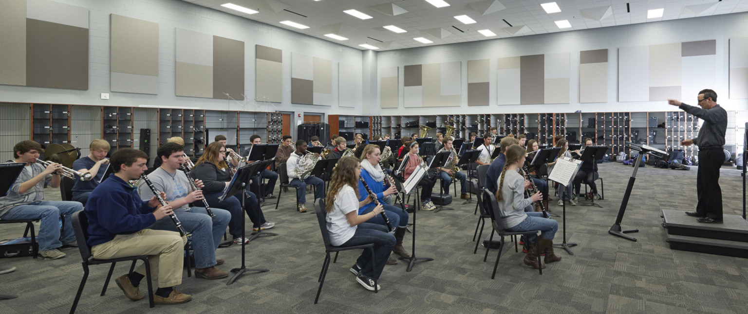 Students practice in band room with colorblock grey, brown, and beige acoustical panels on walls. Bottom of wall has lockers