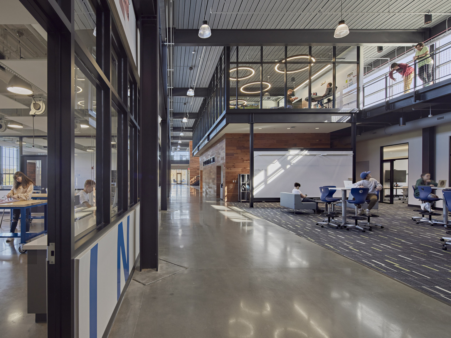wide view of an industrial architecture where a wood working classroom next to a collaboration area with a large whiteboard and a second floor balcony connecting students