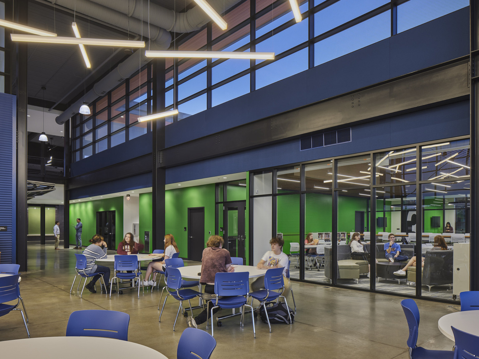 double height lunchroom with upper level windows bringing light into a space with blue furniture and bright green walls, library visible
