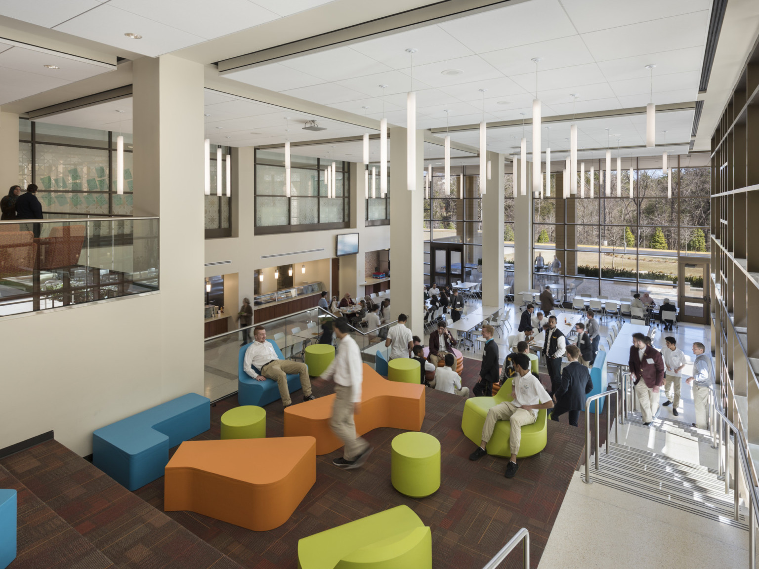 learning stair at a school with colorful, flexible seating, two-story floor to ceiling windows, and a lunchroom at the base of the stairs
