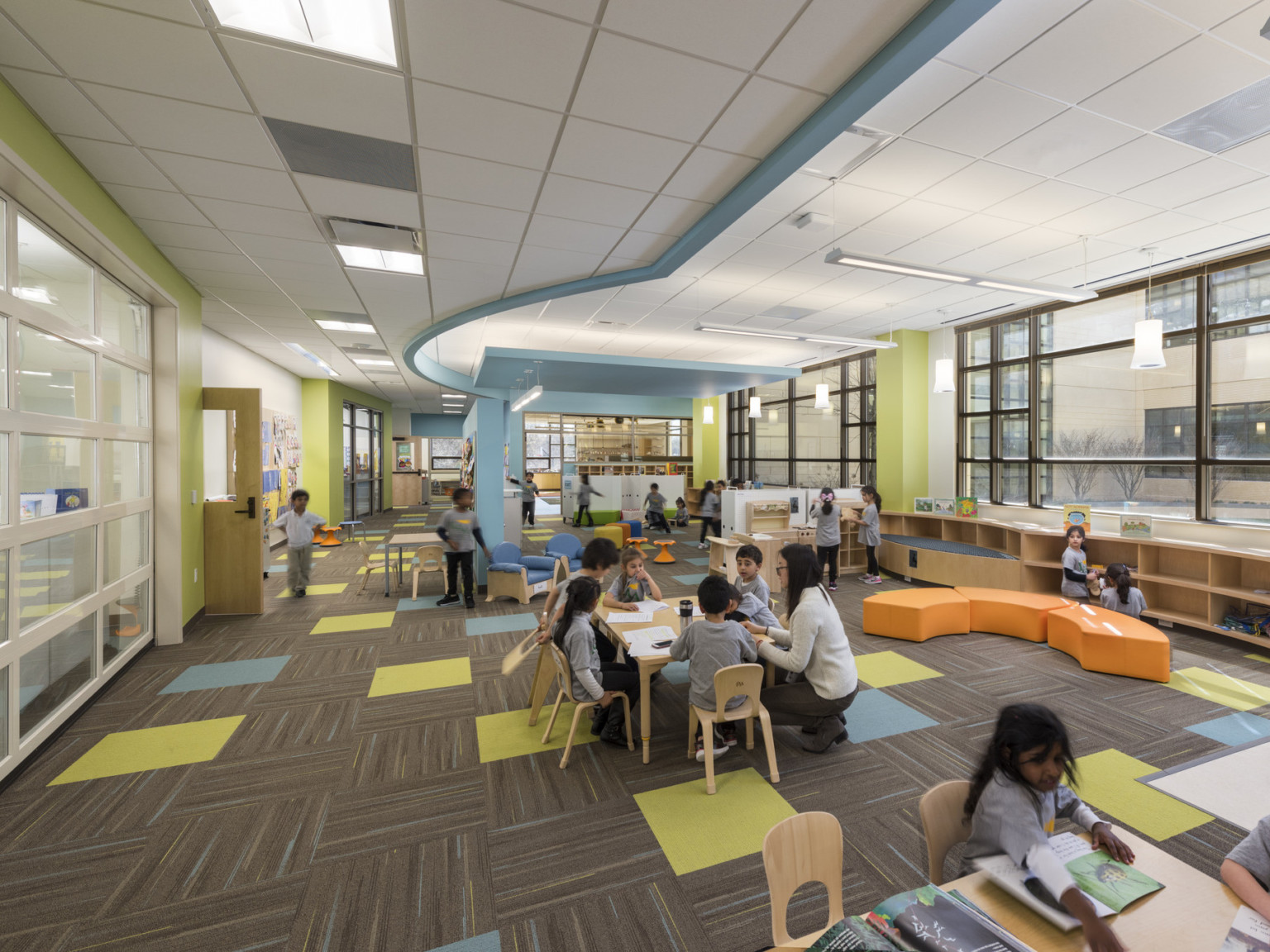 early learning clasroom with colorful carpet, sustainable wood furniture, and color accents on the walls and ceiling to visually identify space
