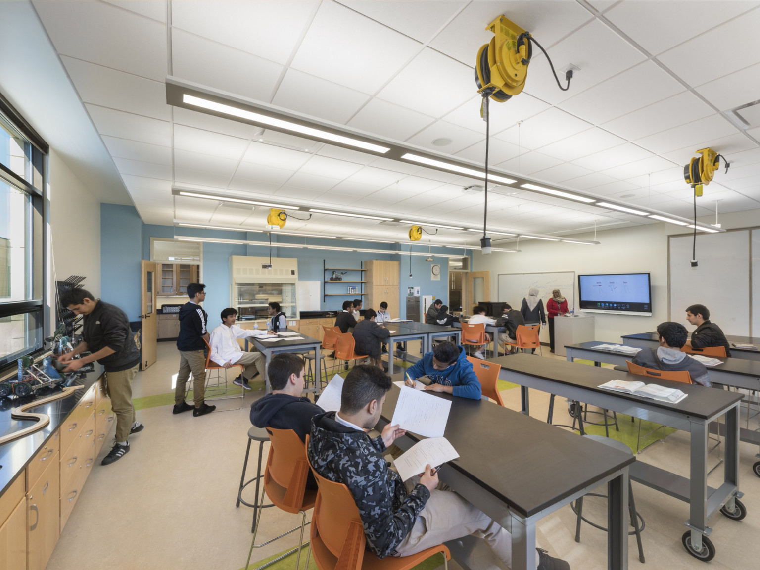 science and tech classroom with accessible power at each moveable desk, a touchscreen, and lab equipment on the far wall