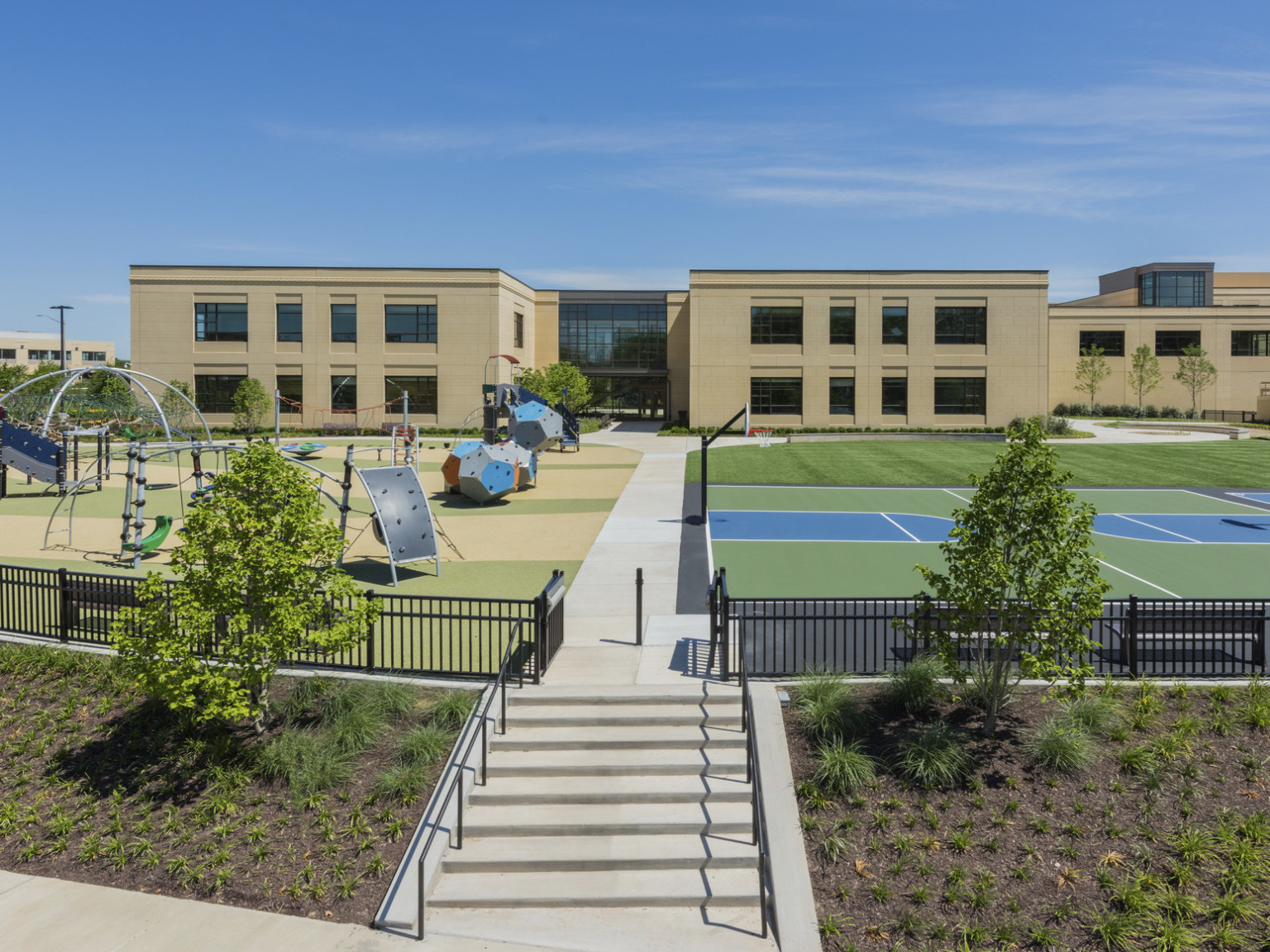 Playground and basketball court outside a two-story school built with a precast concrete façade