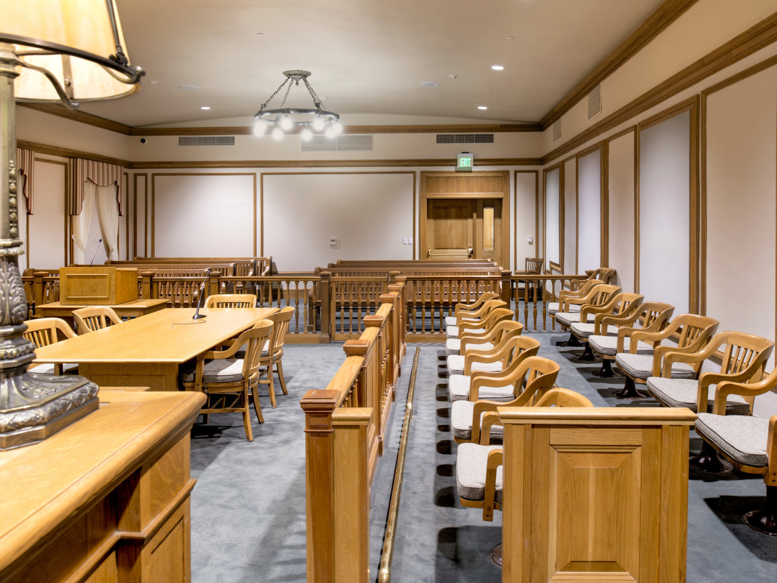 Courtroom with white walls, grey carpet and wood details. Carved bannisters separate jury box and public seating