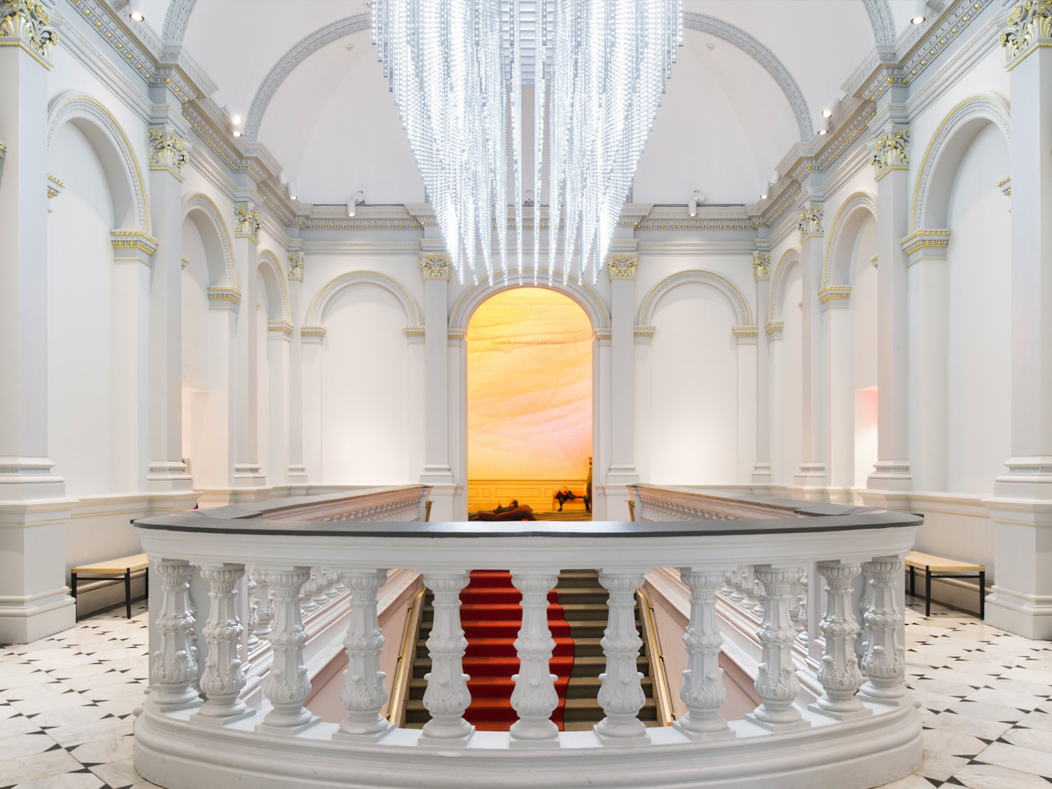 Custom sculptural chandelier hanging parallel above staircase in white room, banister with dark accent in front