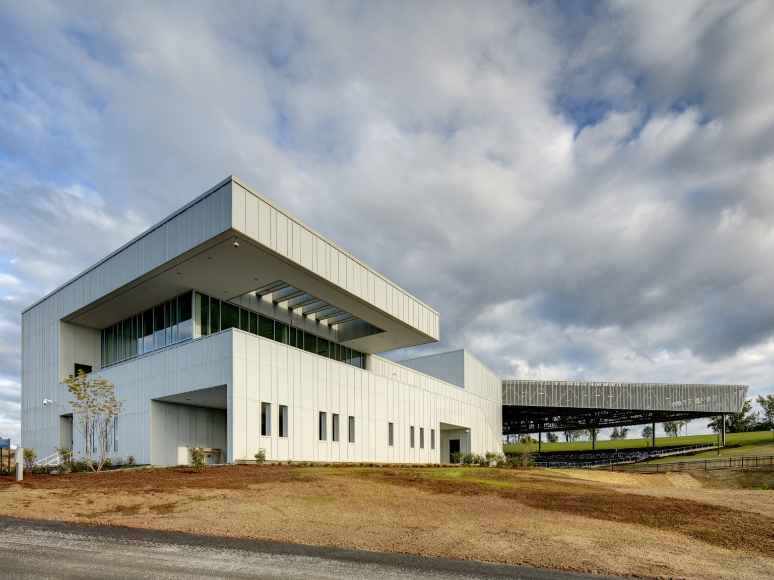 Exterior corner of white building with paneling. Recessed upper level with floor to ceiling windows and overhang with skylight