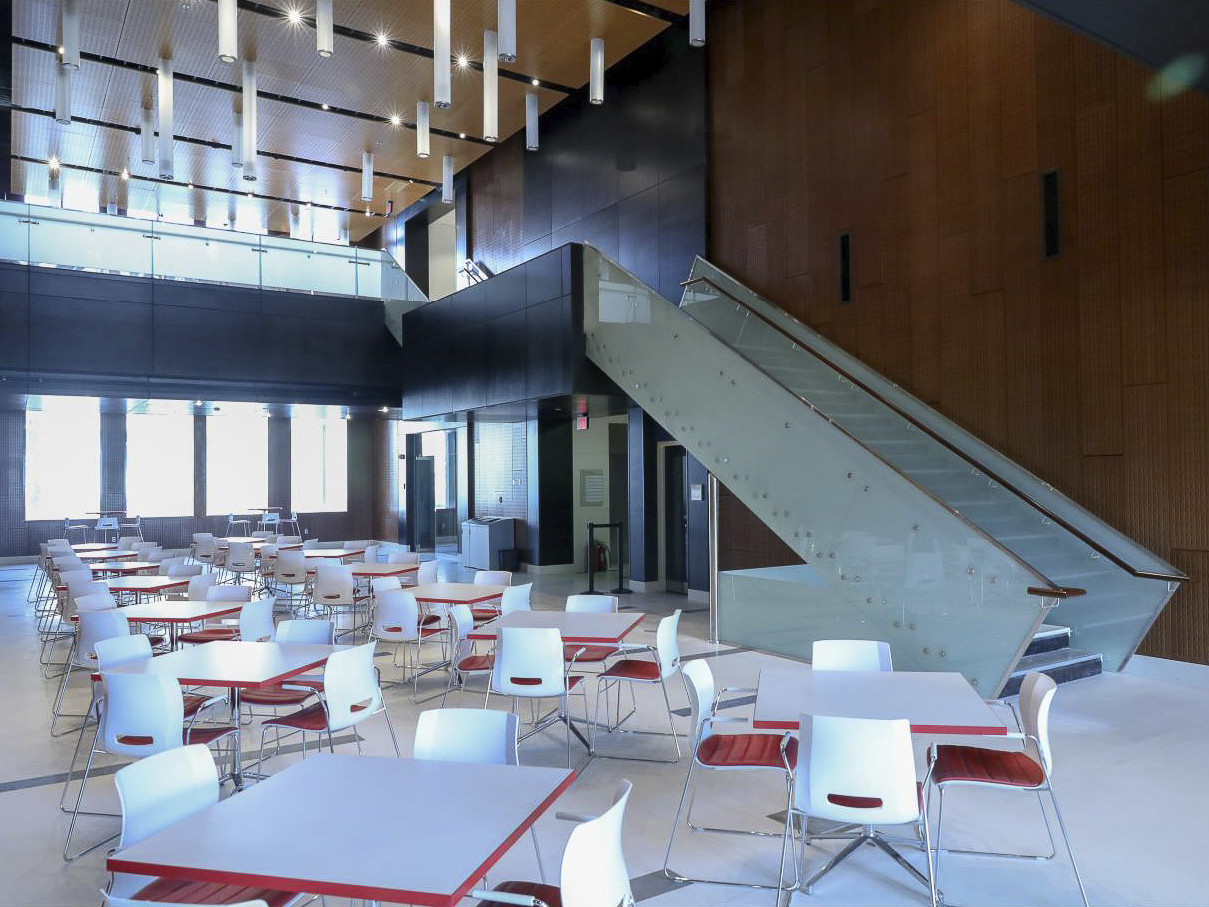 Seating area with white tables and chairs with red accents. Metal staircase to black second floor with hanging lights