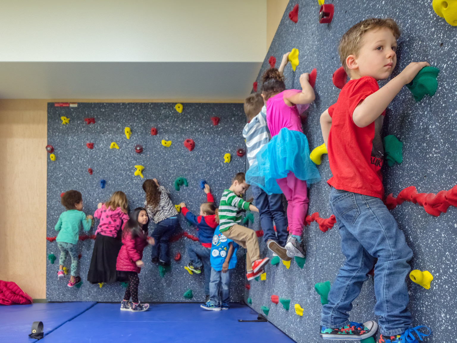 Children using a rock climbing wall above a blue padded mat