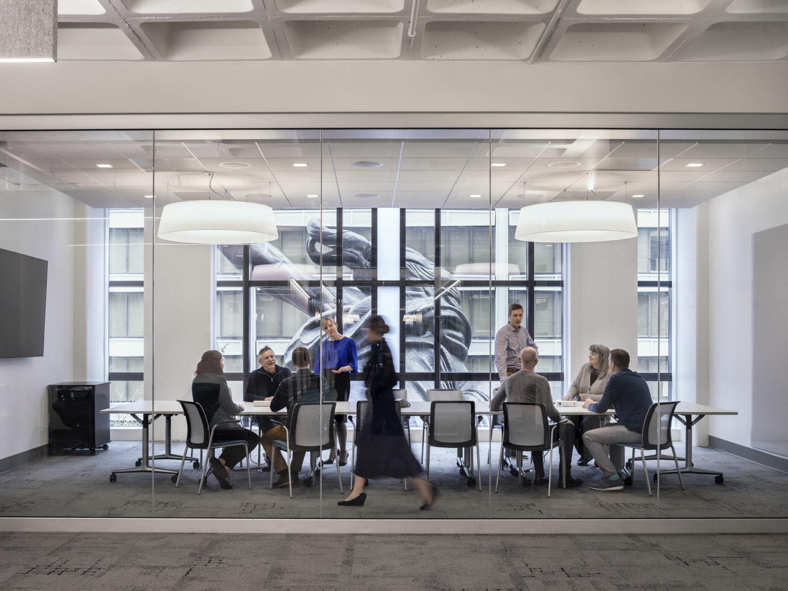 A conference room with glass wall into hallway has floor to ceiling windows looking onto the back of the Portlandia sculpture