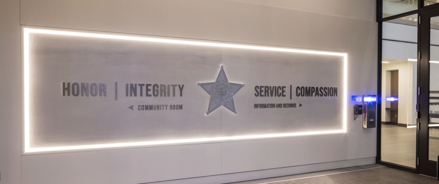 lit wayfinding signage with mottos Honor | Integrity and Service | Compassion on either side of police star above directions