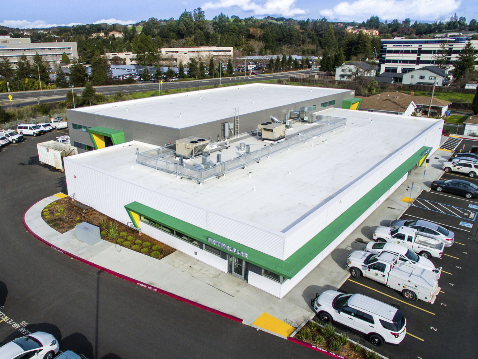 Aerial view of white rooftop on building with green and yellow awnings around entrances. Ducts and air conditioning on roof