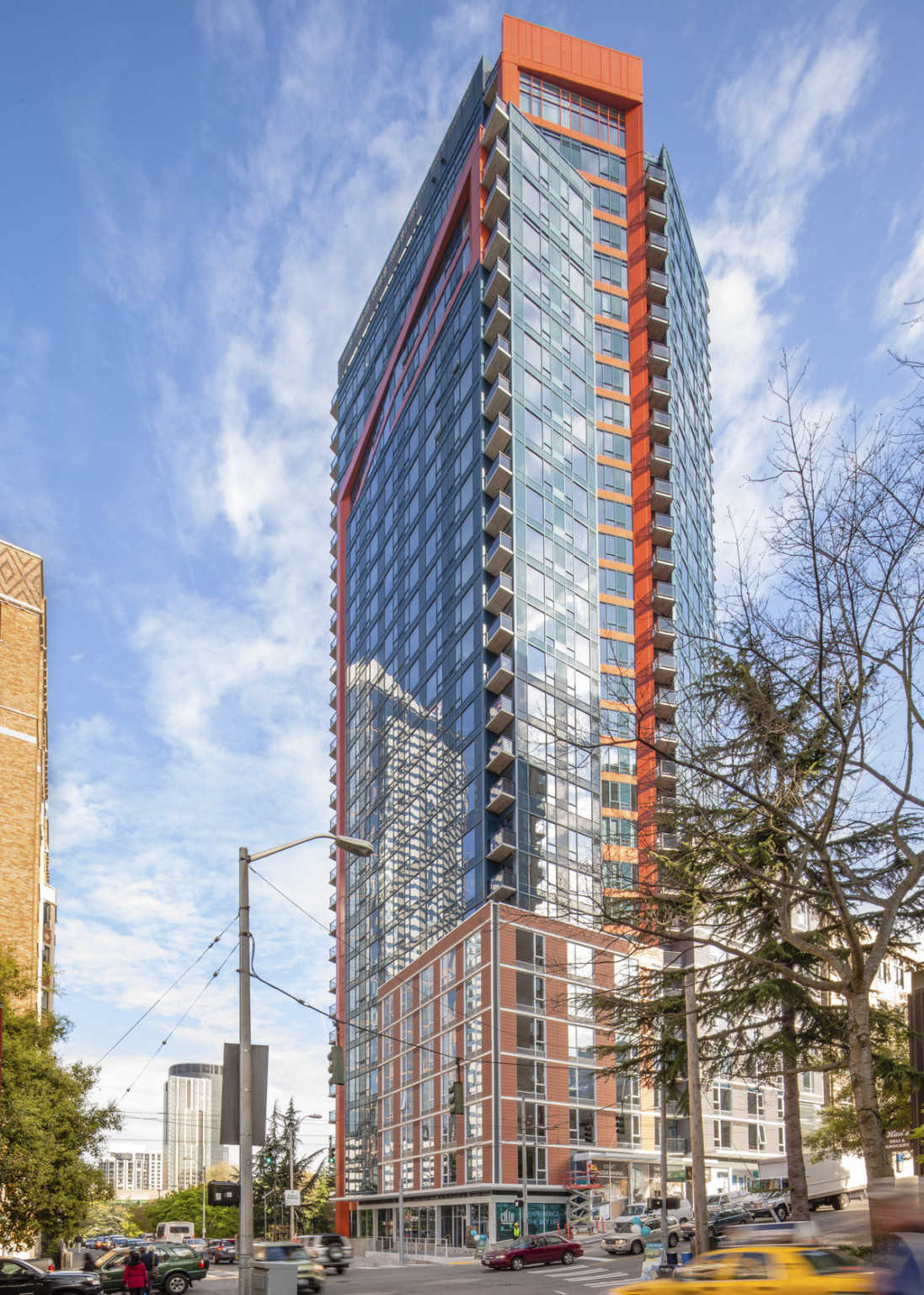 Corner view of a 32 story glass building with brick base. Middle glass wall angles inwards to recessed orange facade