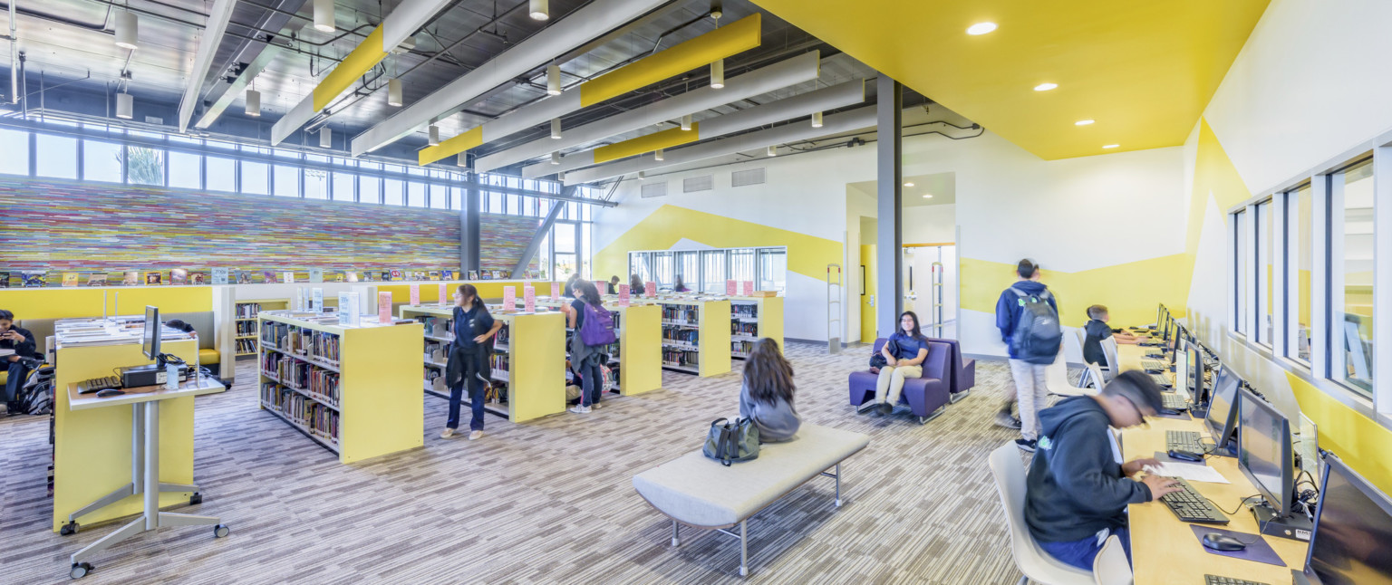 Yellow half height bookshelves in room with yellow stripes on white wall and colorful abstract pattern, left. Computers right