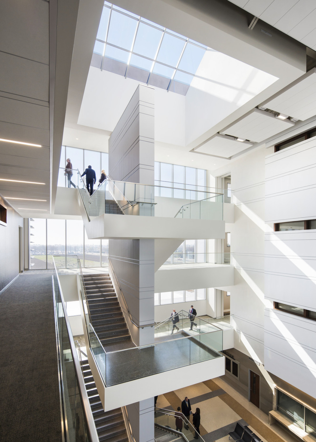 Stairwell in 4 story atrium with floor to ceiling windows at front and skylight above. Grey striped central wall in stairwell