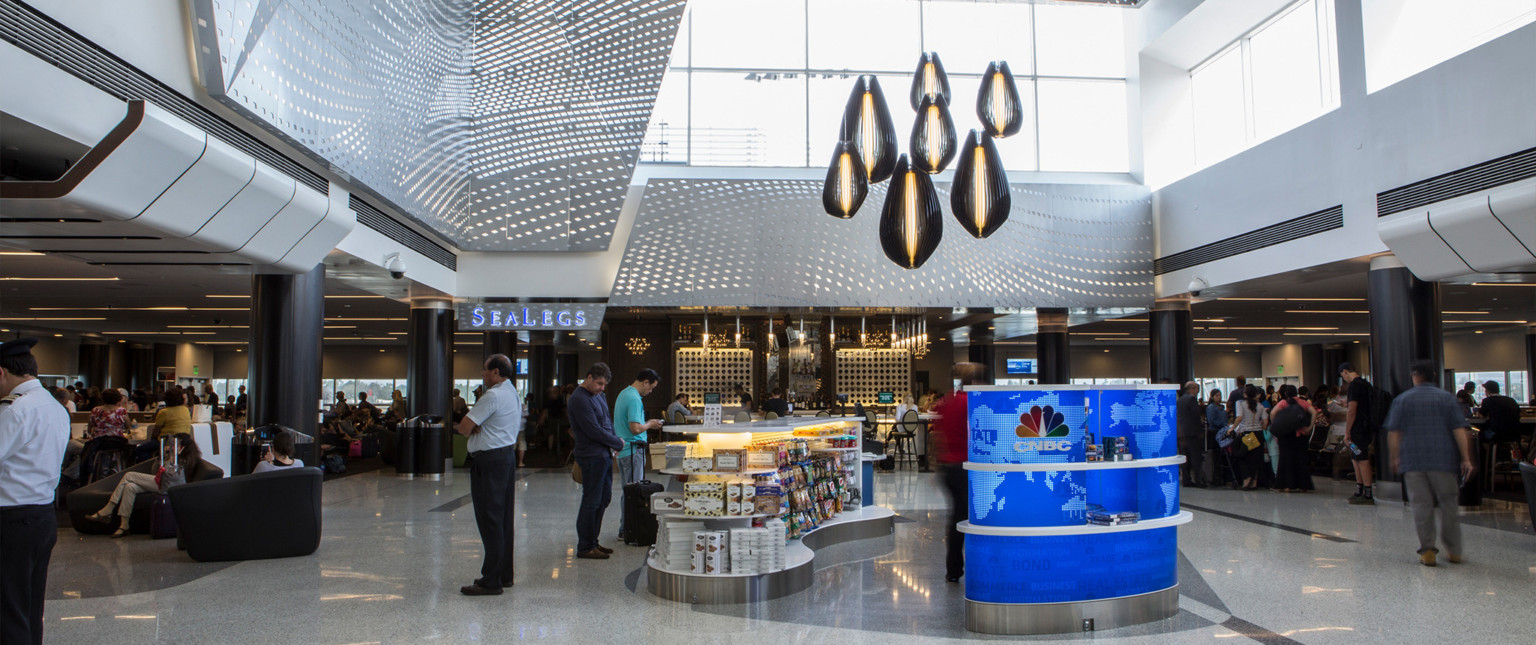 Pendant lights above kiosk in double height room. Large windows (front, right), silver perforated panel accents (front, left)