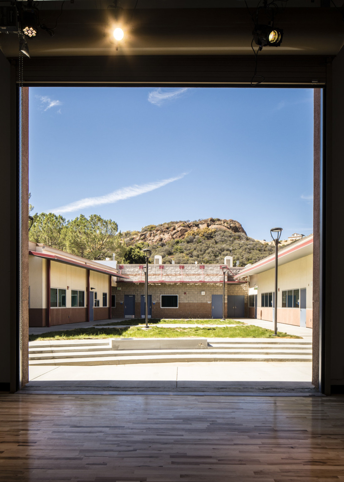 Hardwood floor room with large square opening looking across courtyard to stone buildings in front of Malibu Hills