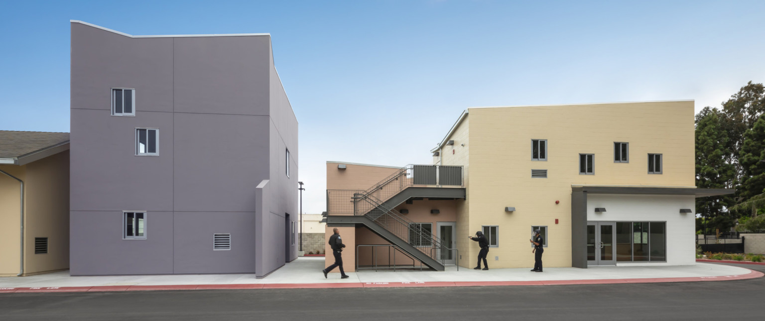Officers participate in hands on scenario training at peach colored two story lab building with stairwell in front
