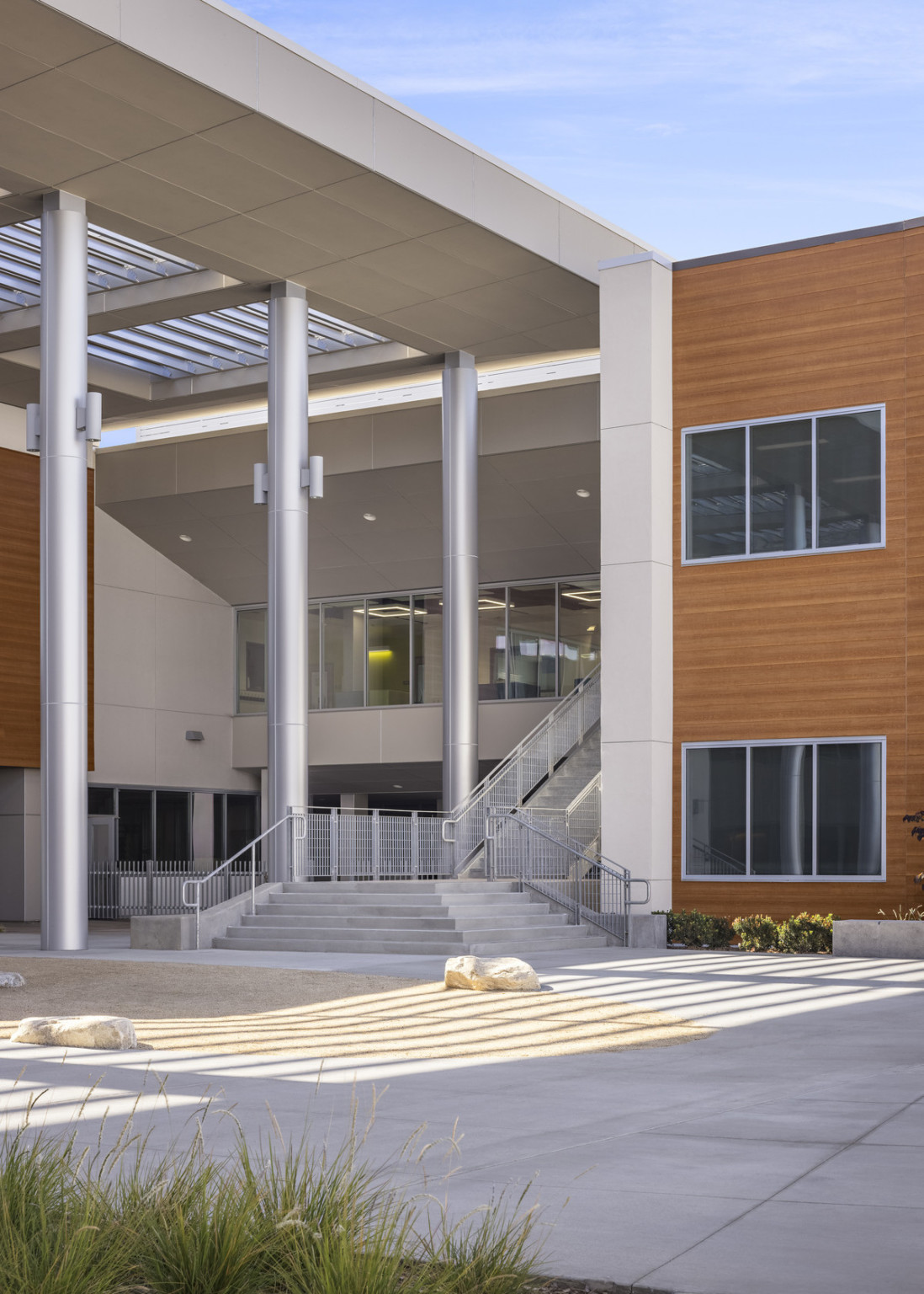 Closeup of stairs to recessed second level entry with floor to ceiling windows. White pillar, right, and wood paneled wall