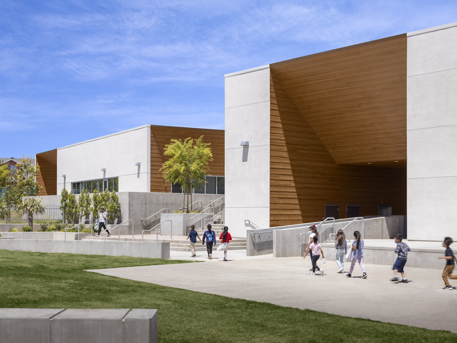 Side exterior of building. Right section has white front with angled recessed wood section in the middle. Ahead are the steps