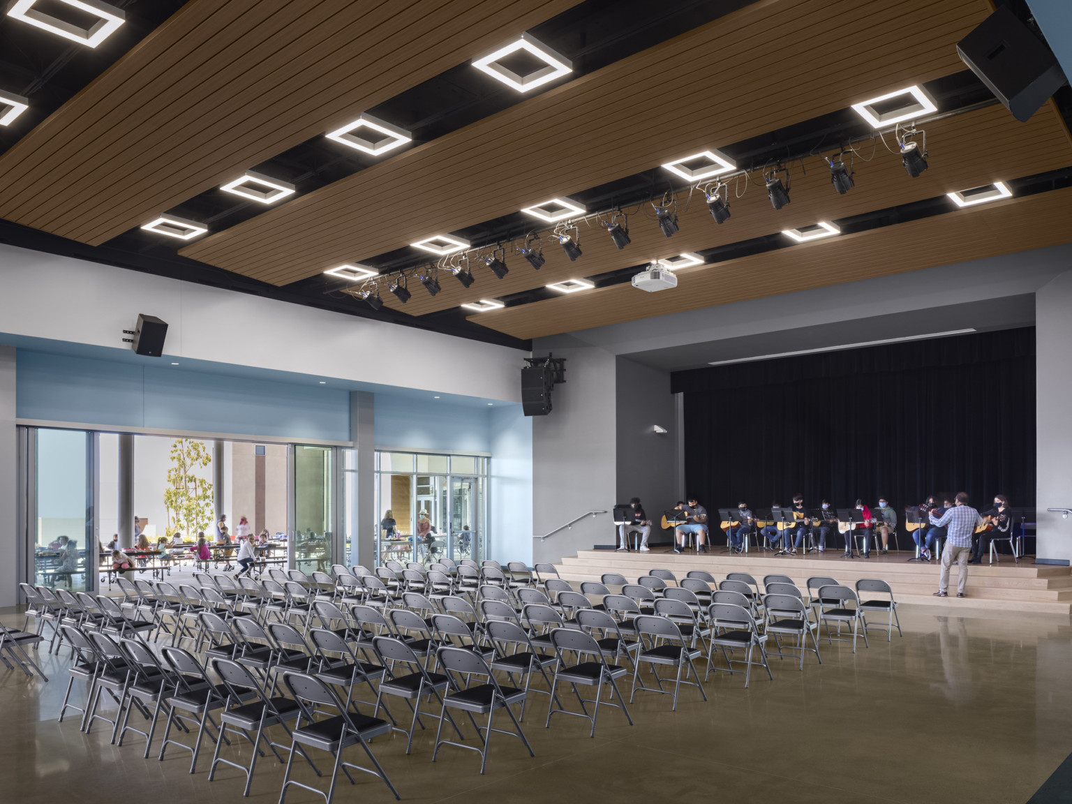 View of stage from opposite corner. Left is floor to ceiling windows. The space is now filled with folding chairs