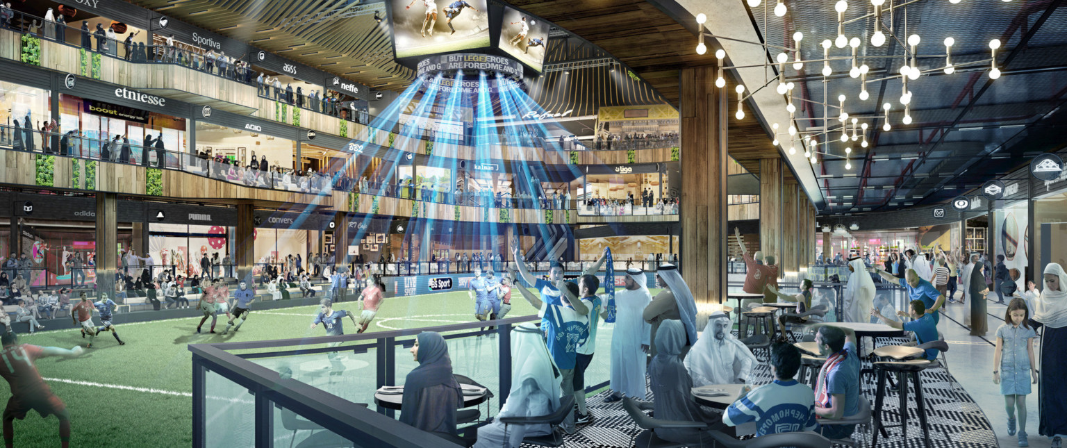Soccer field in a triple height atrium. Seating on sidelines with tables. Above, walkways on 2nd and 3rd floors with shops