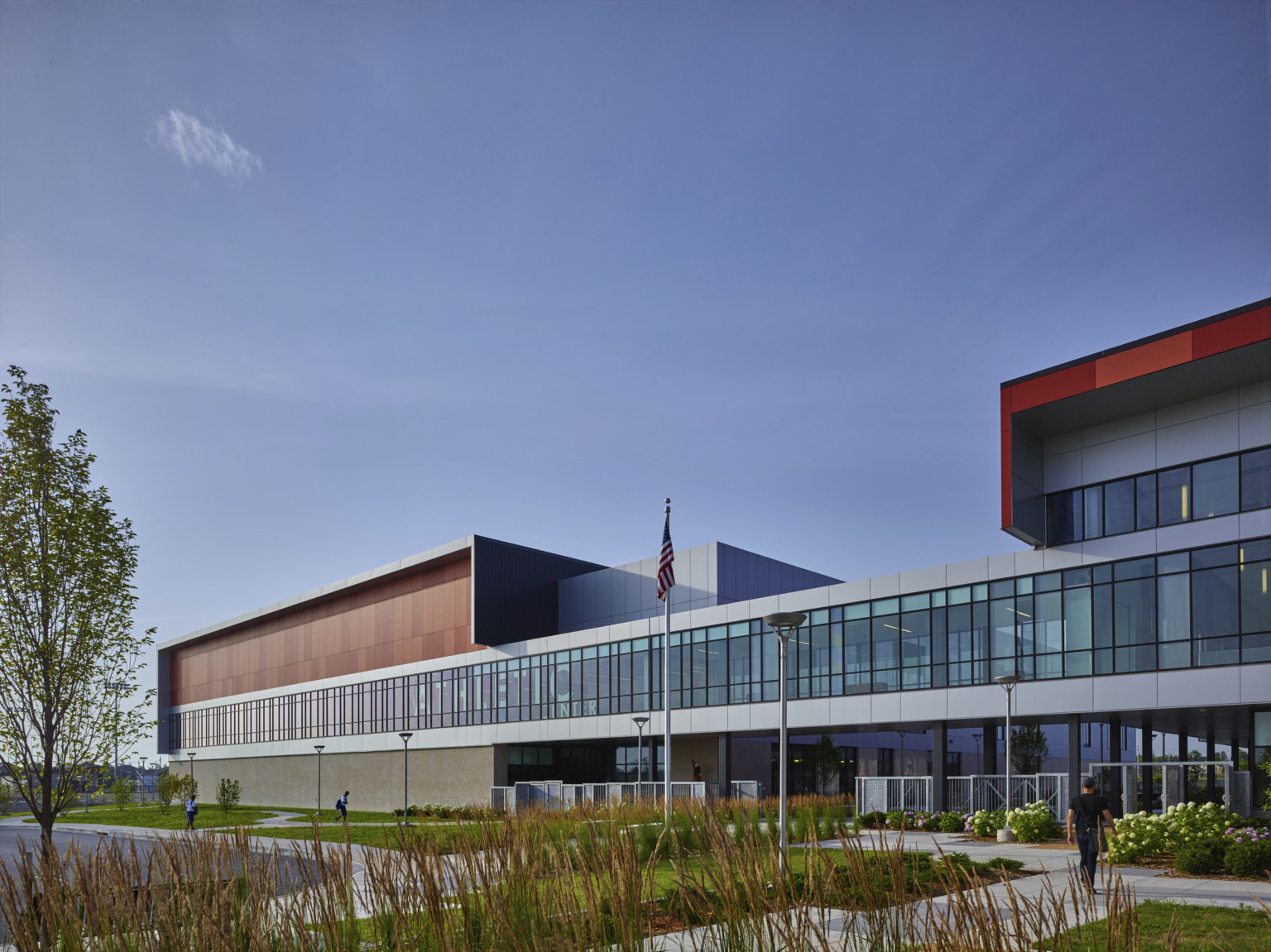 high school with glass and brick facade and tall native grass landscaping with sidewalks crossing through