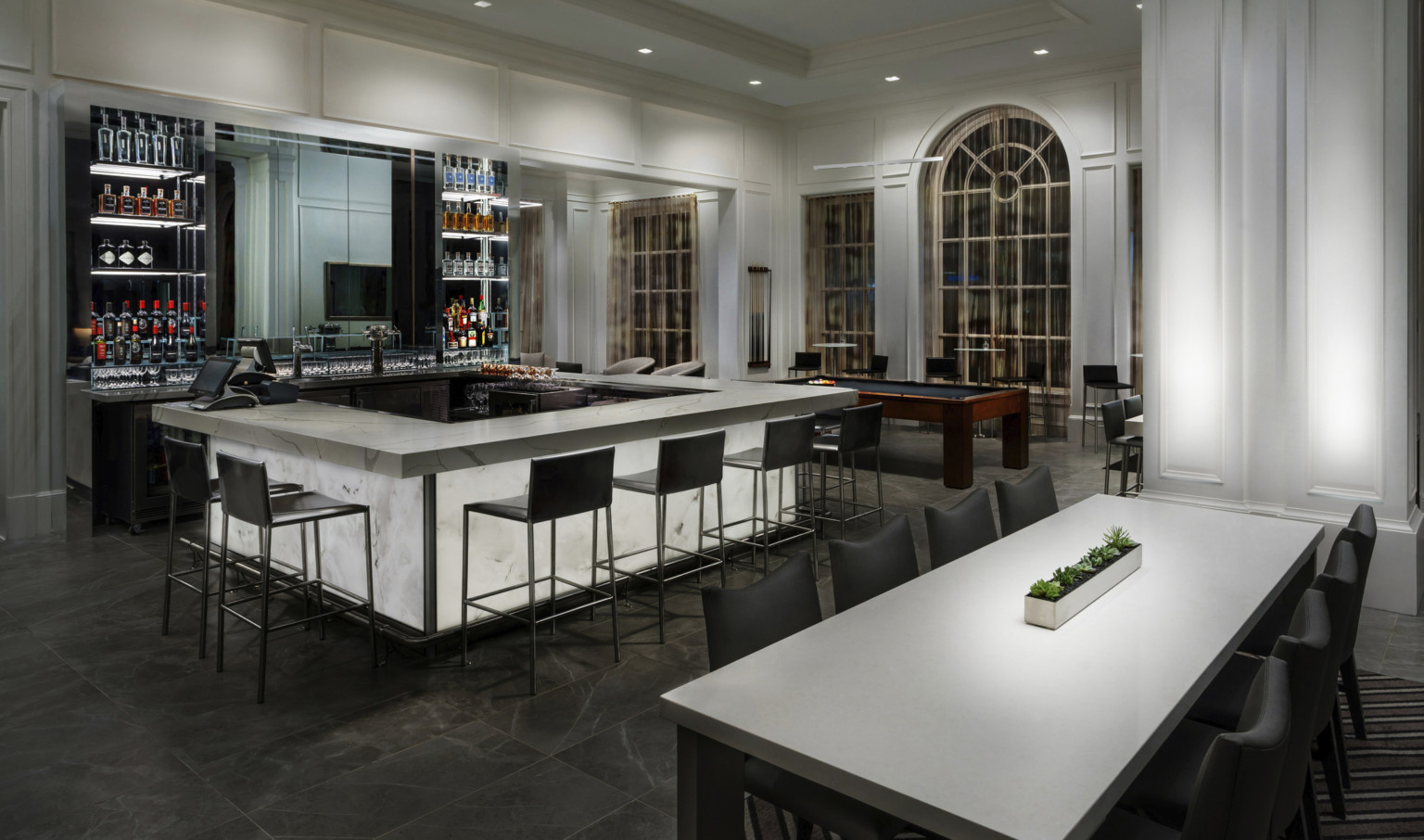 Marble patterned bar with base illuminated from within in white room with arched window. Black built in shelves behind bar Marble patterned bar with base illuminated from within in white room with arched window. Black built in shelves behind bar