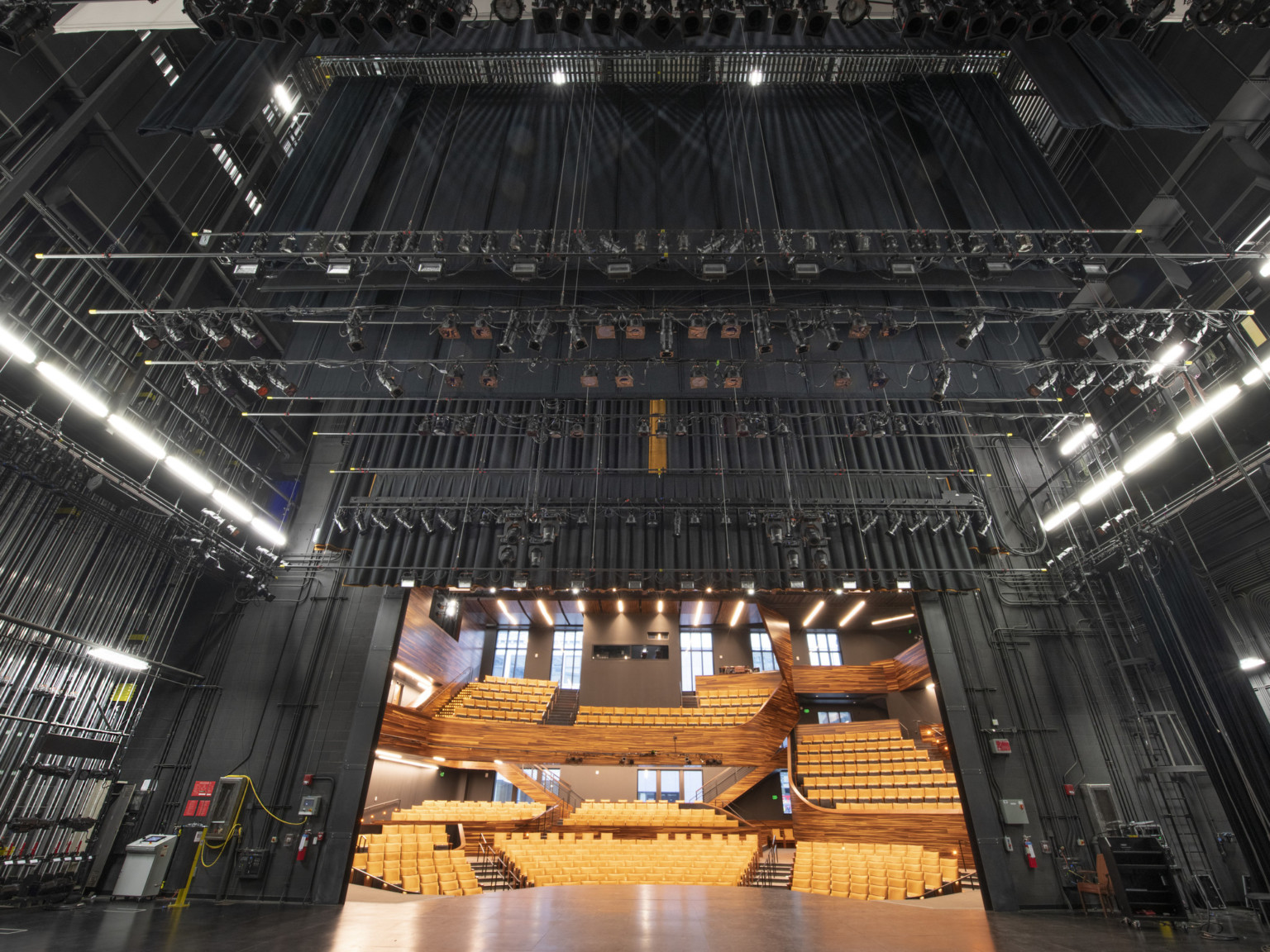 Looking from backstage outwards to dark colored stage rigging system hidden from yellow empty audience seats