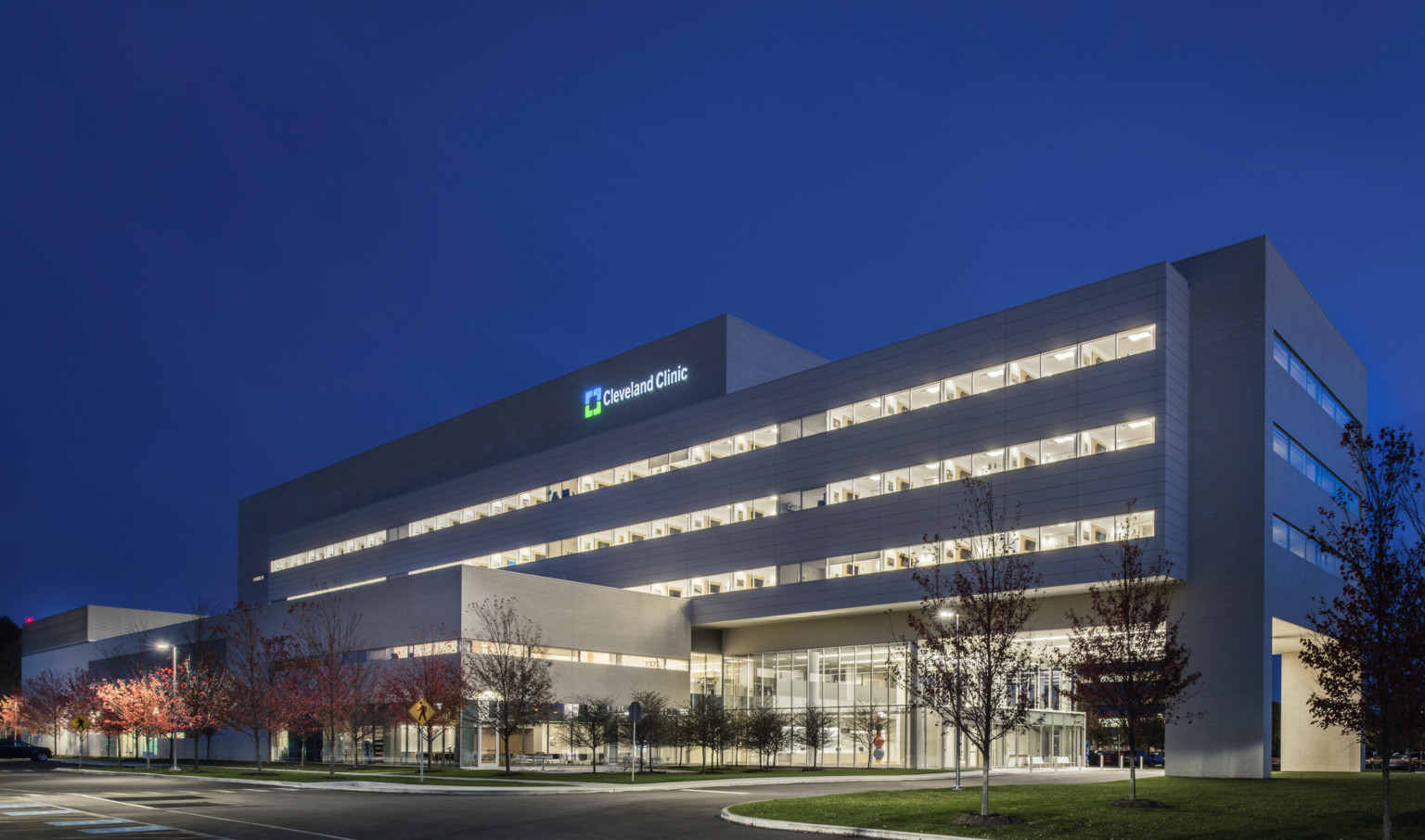Cleveland Clinic Avon Inpatient Bed Tower illuminated at night seen from across the street facing drive up glass doors Cleveland Clinic Avon Inpatient Bed Tower illuminated at night seen from across the street facing drive up glass doors